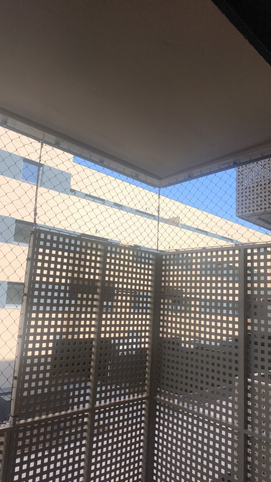 Balcón con celosía de hormigón y malla de protección blanca contra el cielo